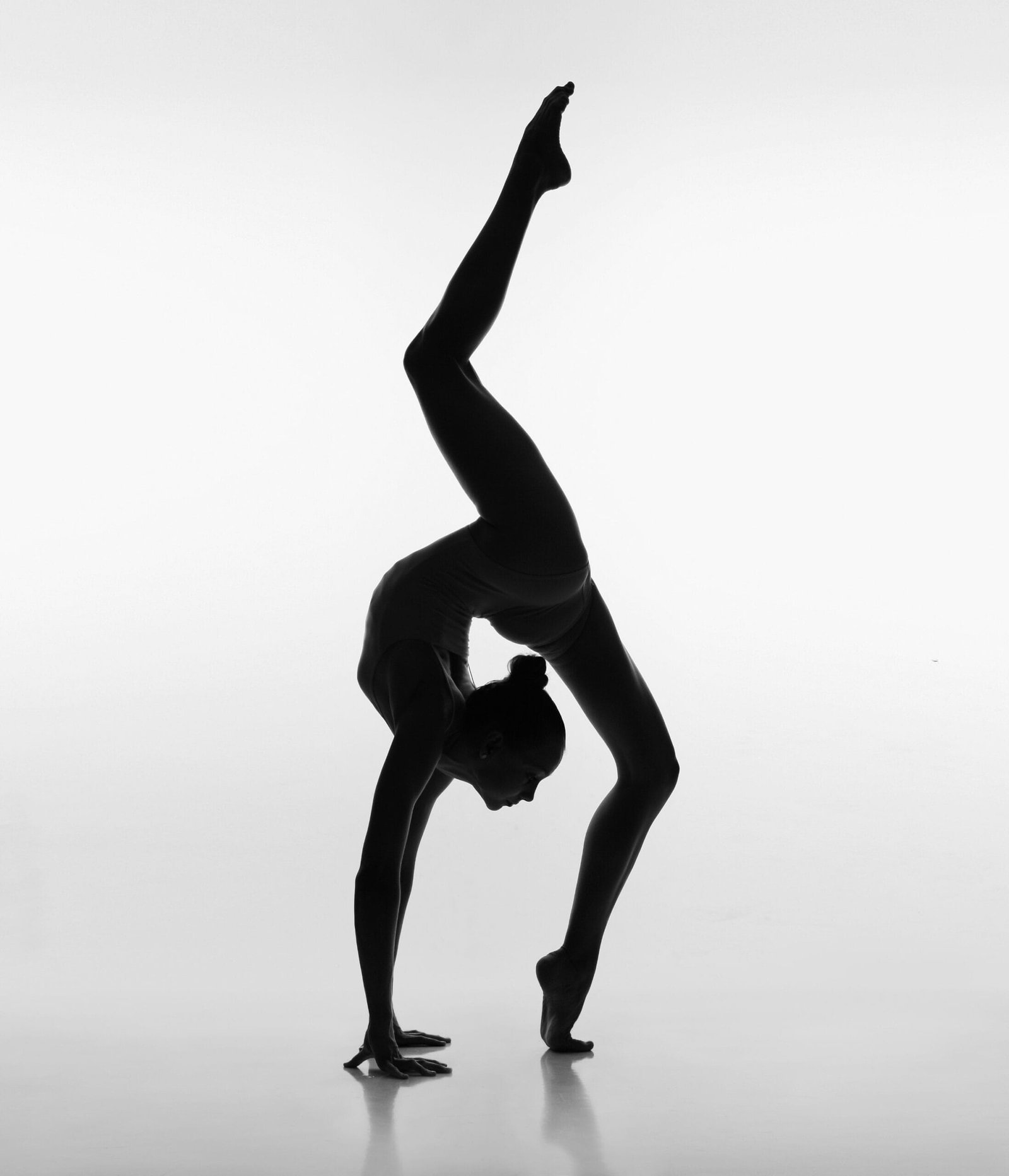 Dancer holding an acro balance in silhouette against studio lighting