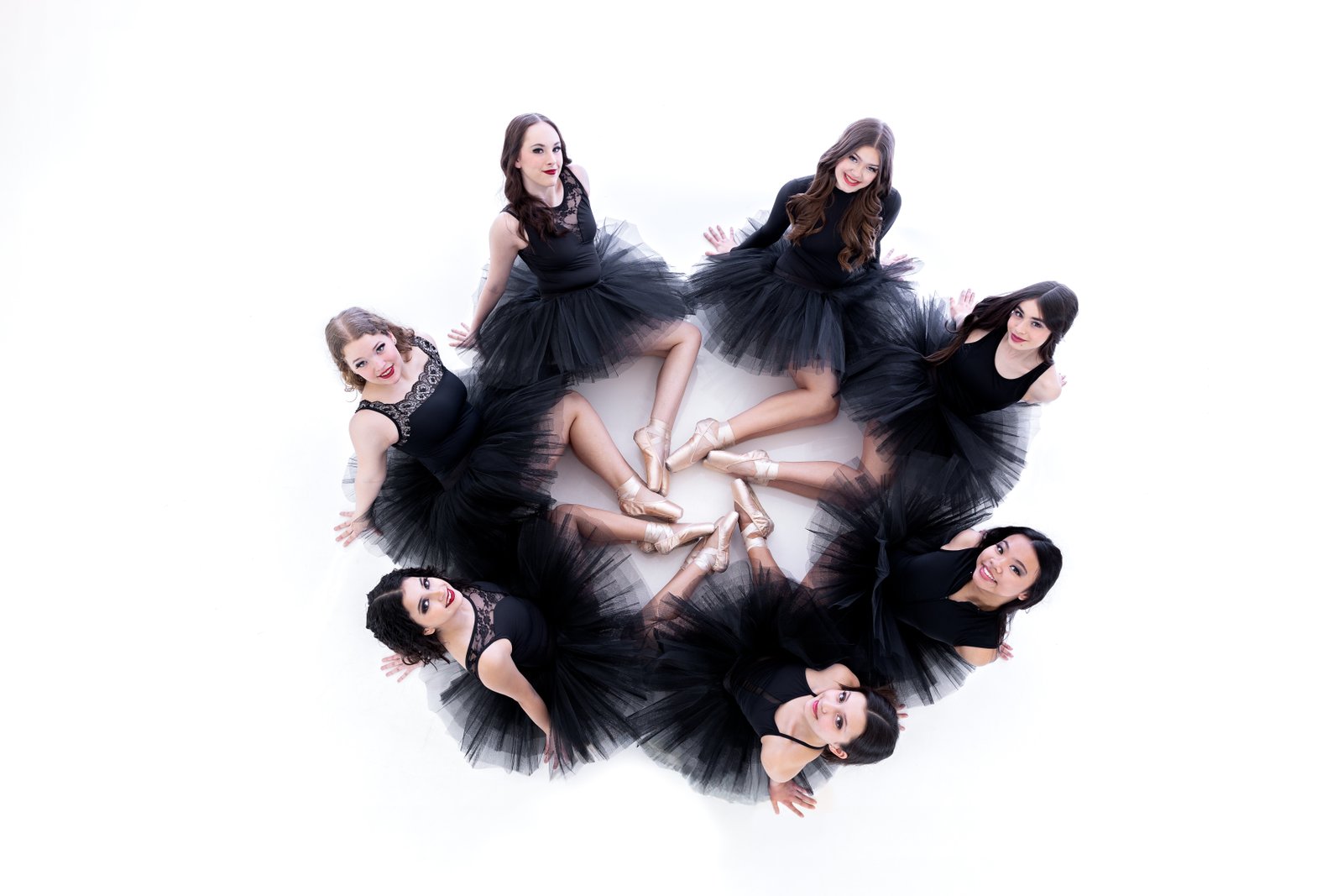 Young ballet students in tutus gathered in a circle on the studio floor